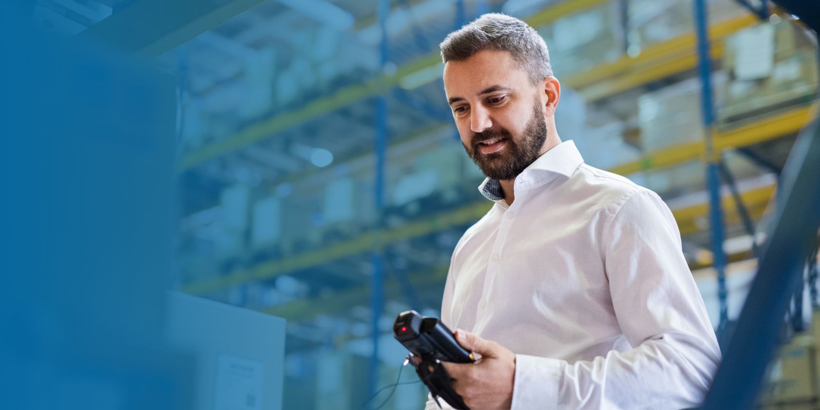 Gerente o supervisor de almacén con camisa blanca, utilizando un escáner handheld de código de barras para registrar datos en el área de estanterías.