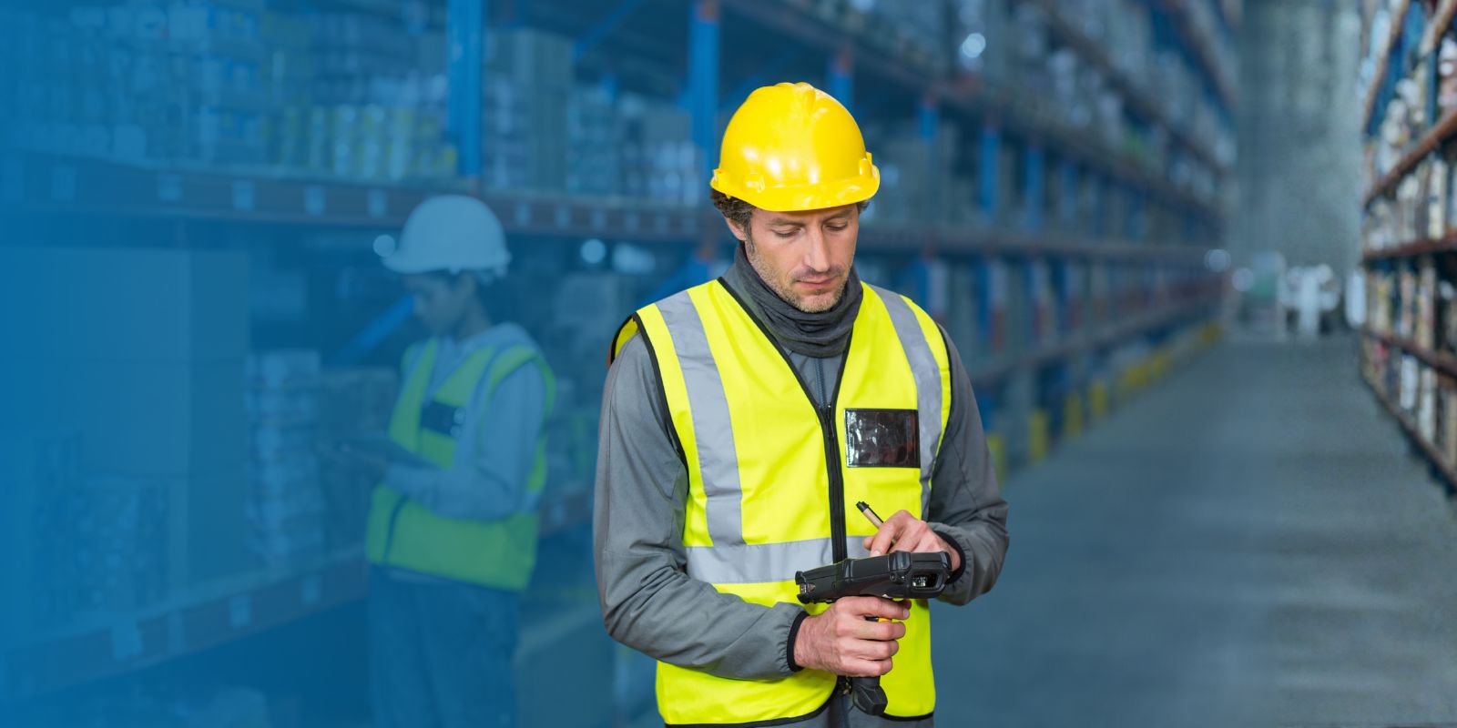 Trabajador de almacén con casco amarillo y chaleco reflectante, usando un dispositivo handheld con escáner para gestionar el inventario.