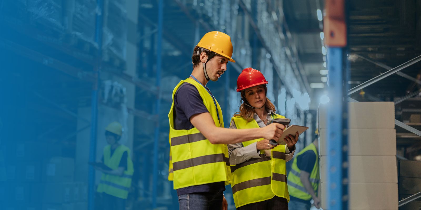 Dos trabajadores de almacén con cascos y chalecos reflectantes, usando un escáner handheld y una tablet para realizar un conteo físico de inventario.
