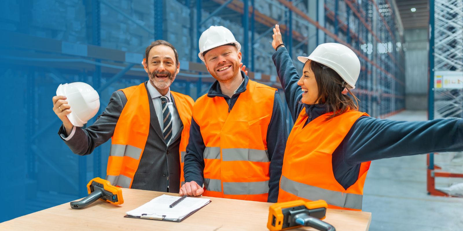 Gerente, supervisor y operaria celebrando el éxito de la gestión de inventario, con dispositivos handheld de escáner sobre una mesa en un almacén.